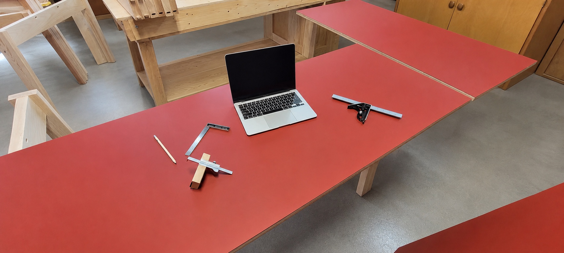 Overhead view of red work surfaces with a laptop and measuring and marking tools