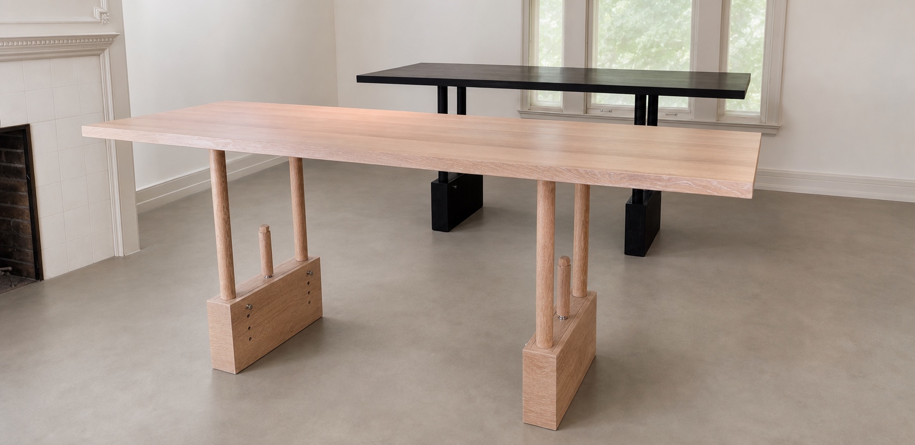 White oak TableRaise in the foreground with a black TableRaise behind it on a concrete floor